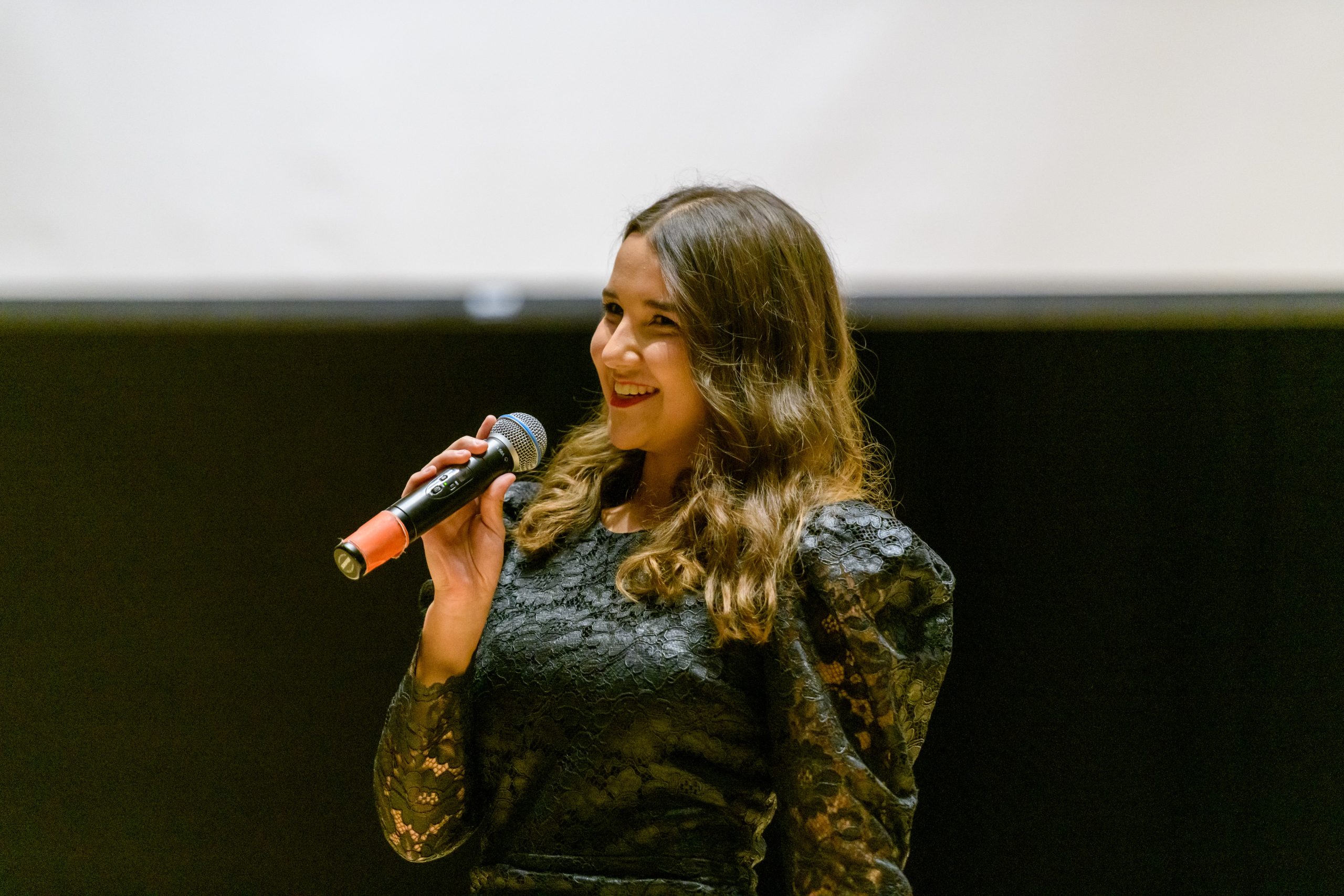 A young woman smiling on a stage with a microphone in her hand