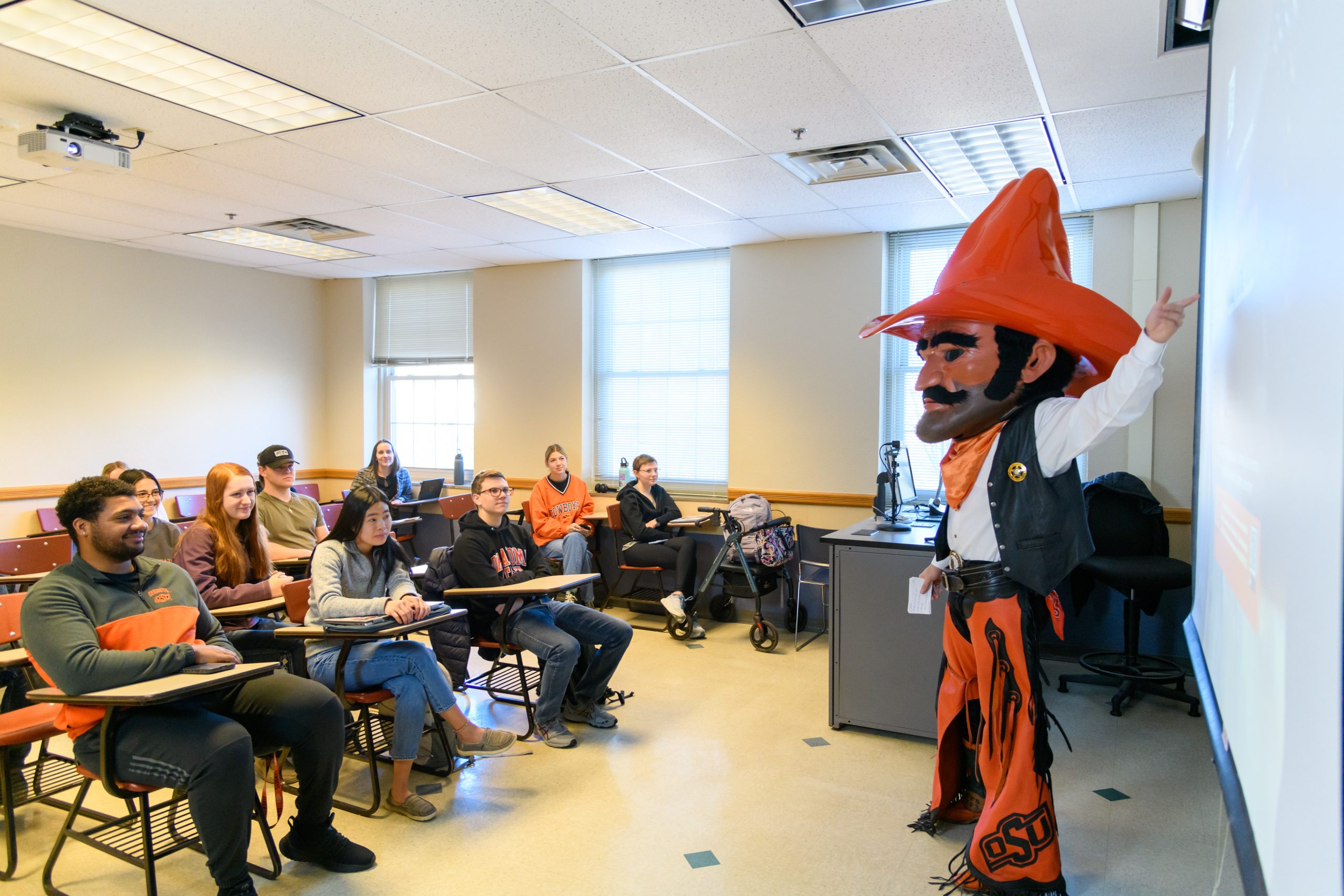 Pistol Pete standing in front of a classroom gesturing to the projector while students are being attentive