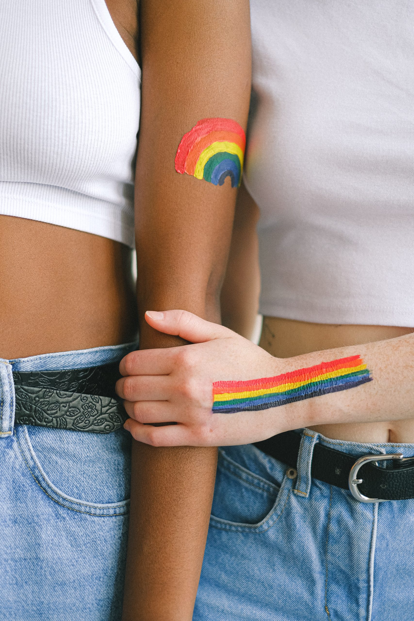 An individual holding another person's arm. Each has a colorful painting on their left arm. One has a rainbow.