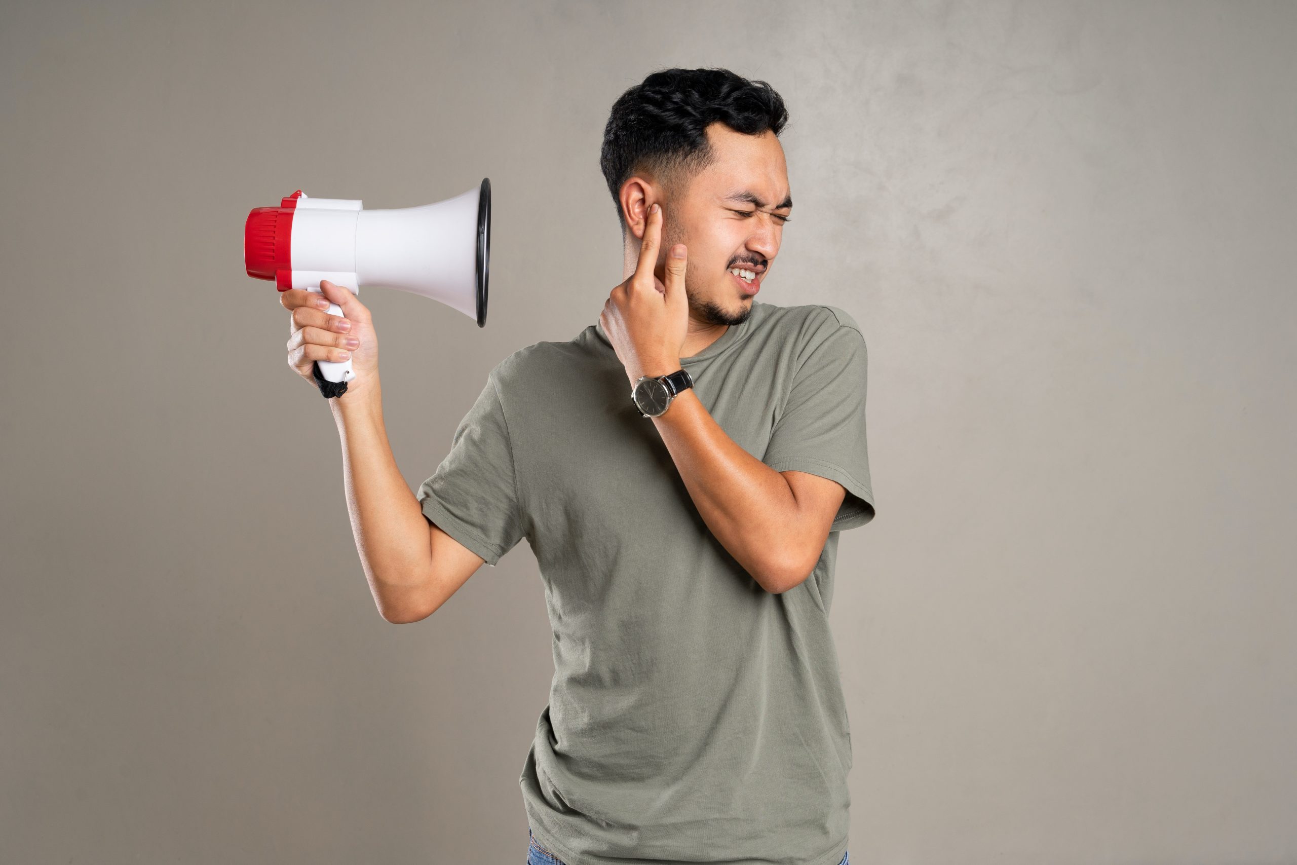 A man holds megaphone close to his head while also holding a finger over his hear to indicate the megaphone is loud.