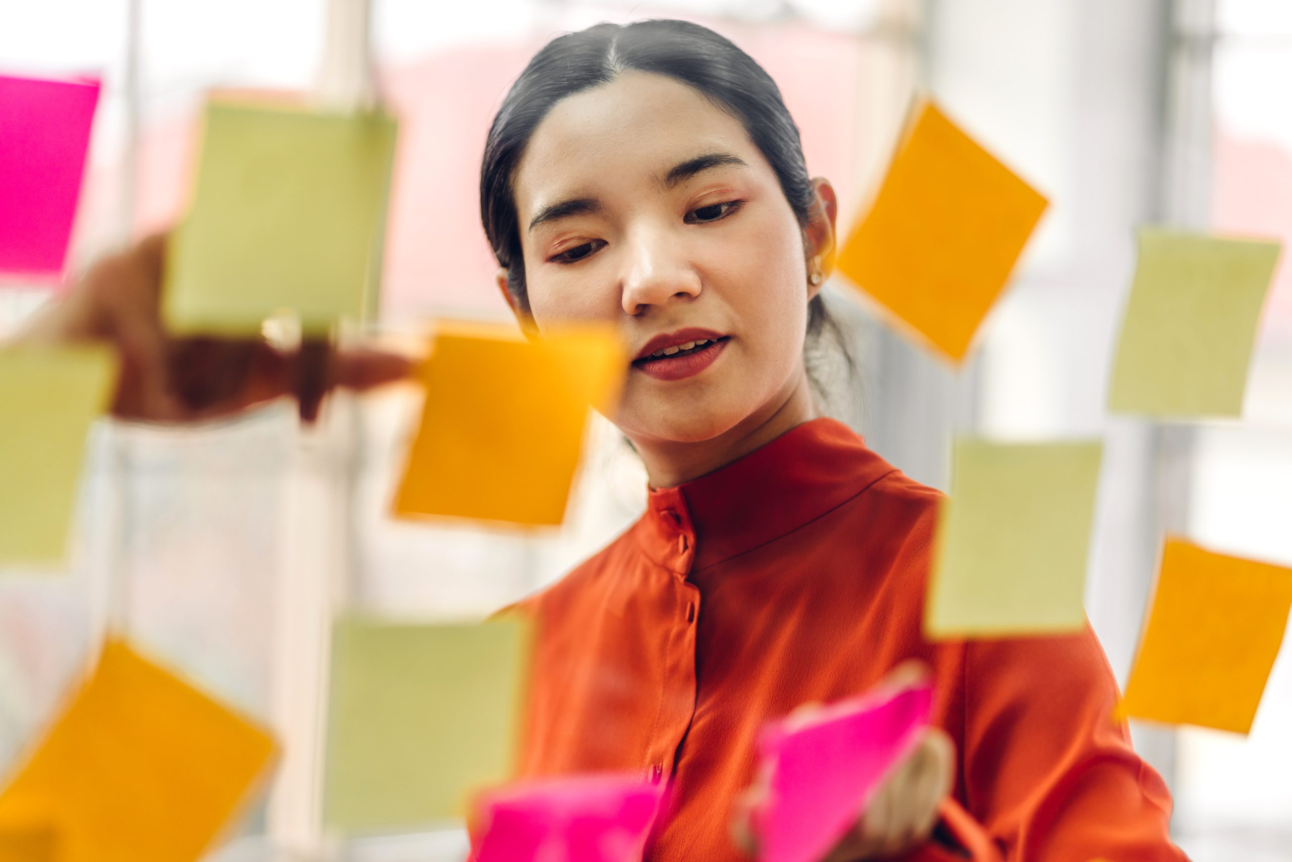 A young female student is studying several Post-it Notes on a glass wall, which contain various forms of support for her presentation.