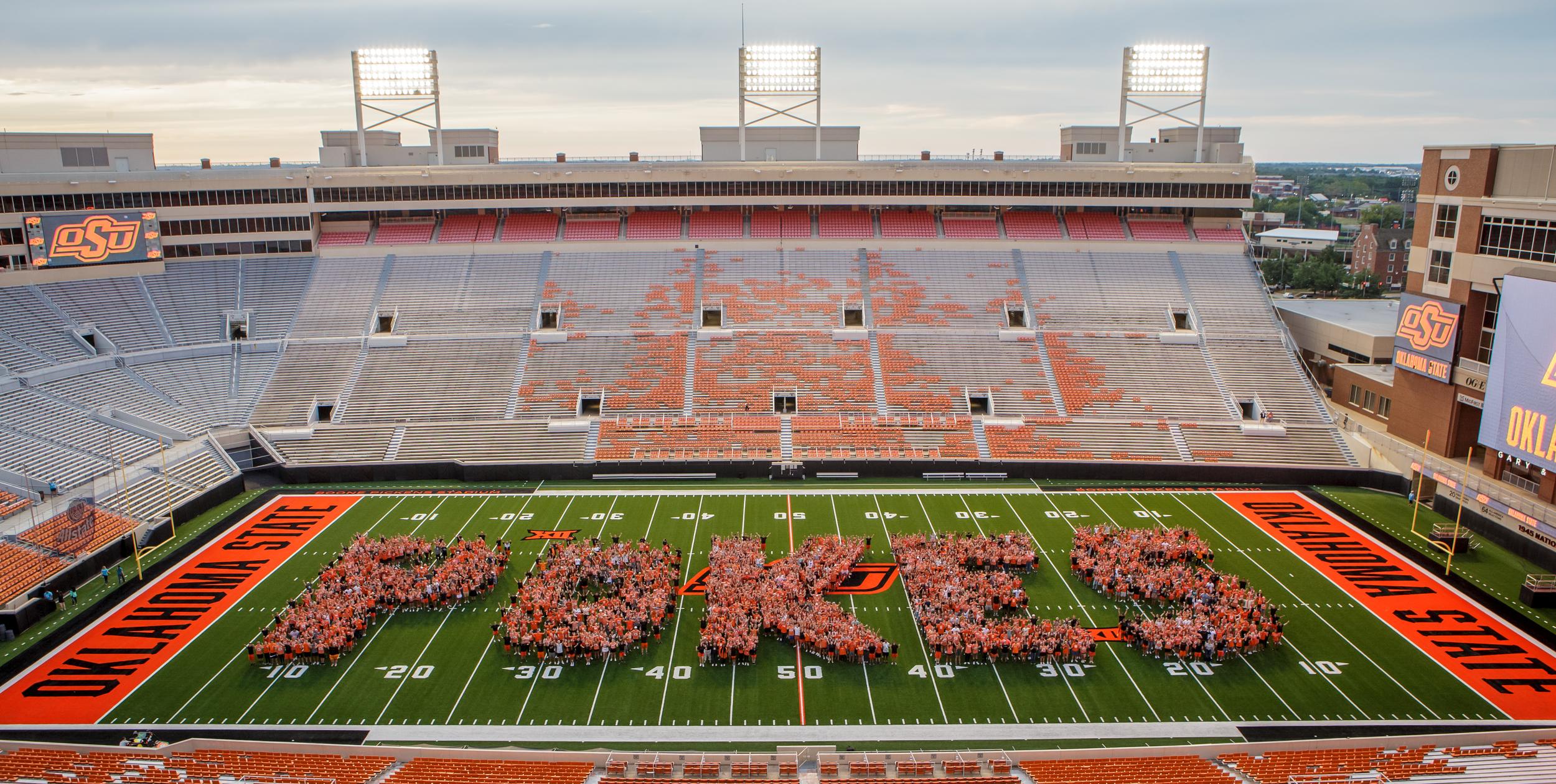 A group of students stand on the field at Boone Pickens stadium and spell out the word, Pokes.
