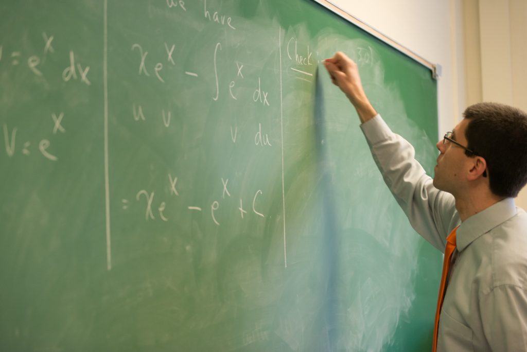 A man writes on a chalkboard using it as a presentation aid.