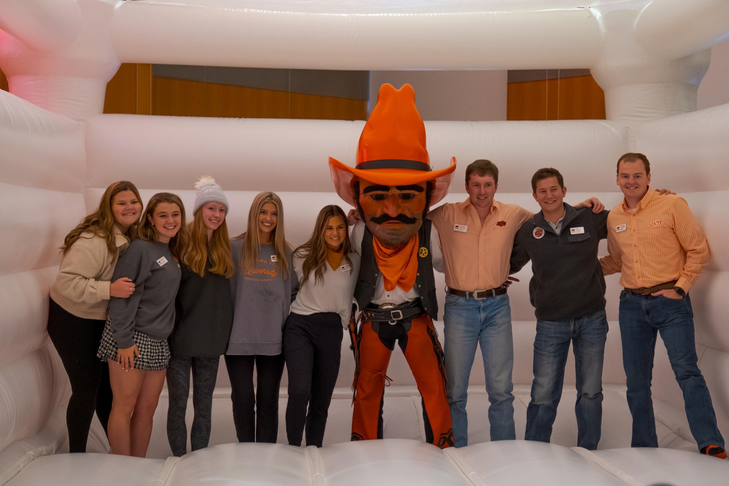 Pistol Pete stands with a group of college students in a bouncy house.