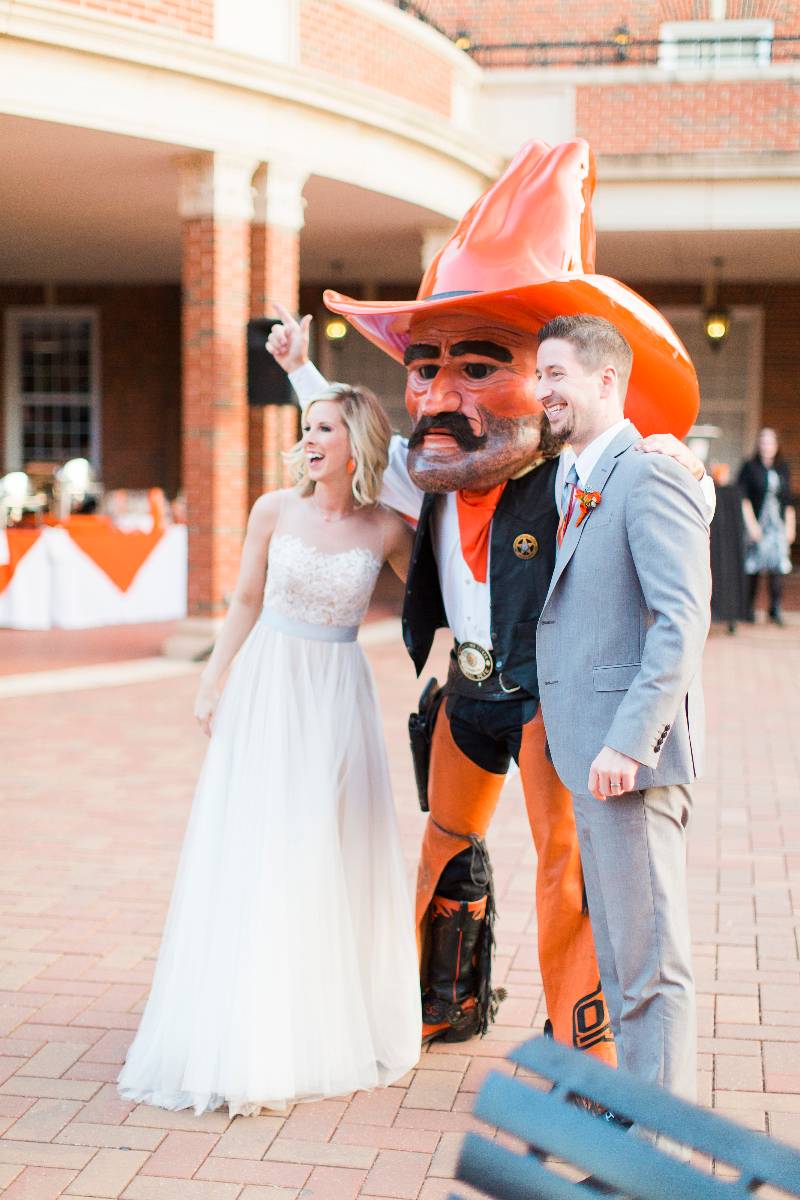 Pistol Pete is standing in the middle of a bride and groom at a wedding.
