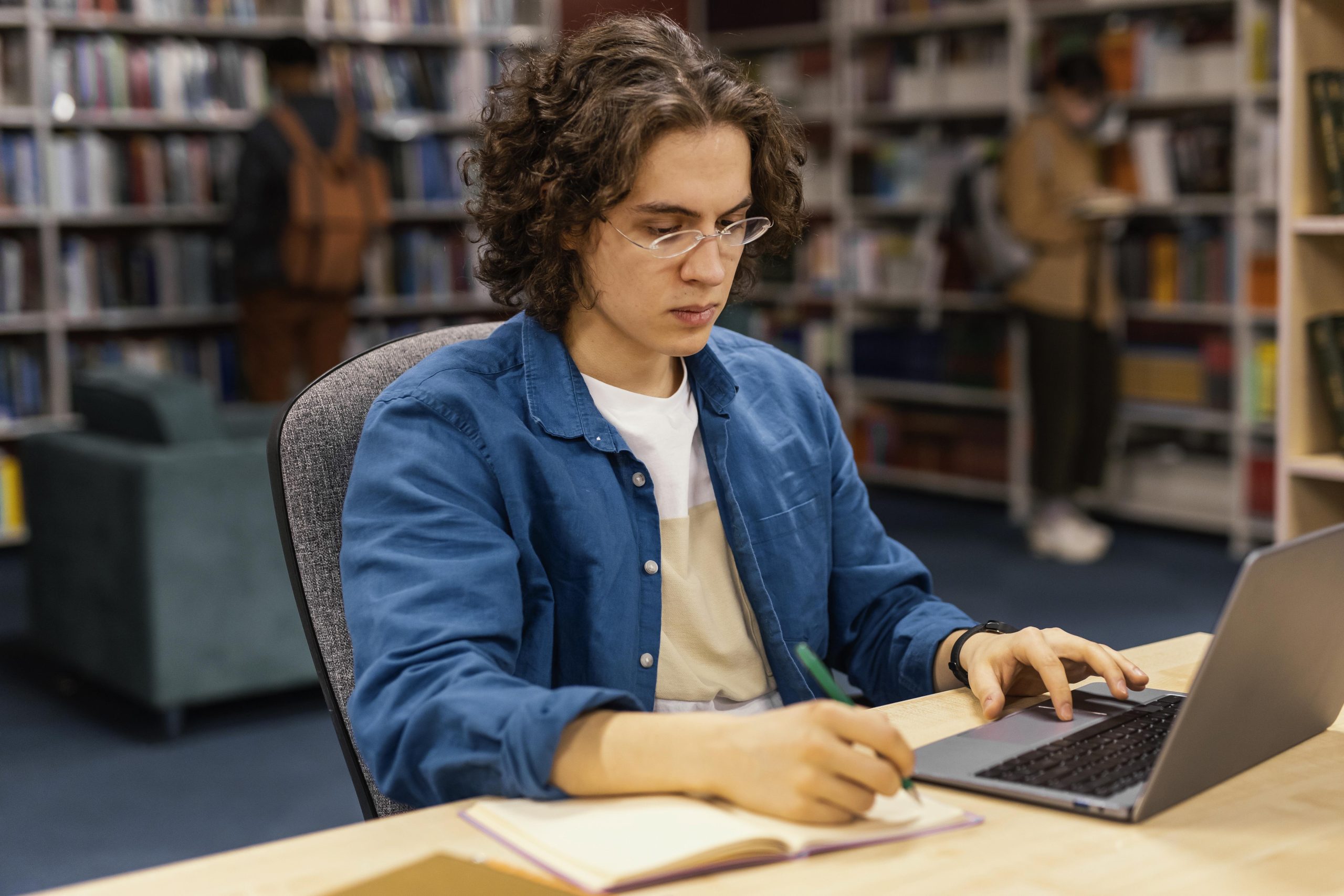 A young man sitting in the library working on his laptop