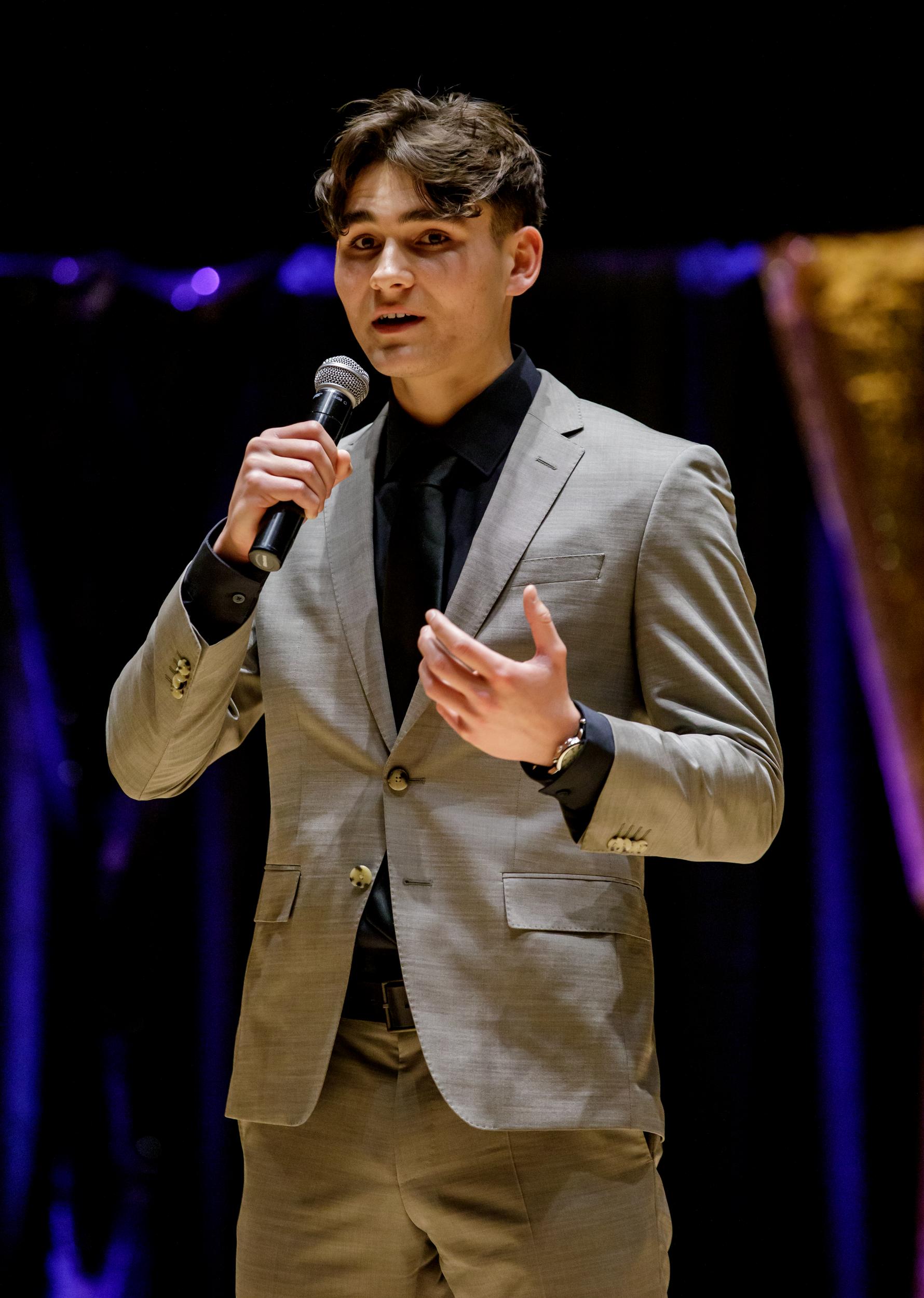 A young man speaks using a microphone to an audience
