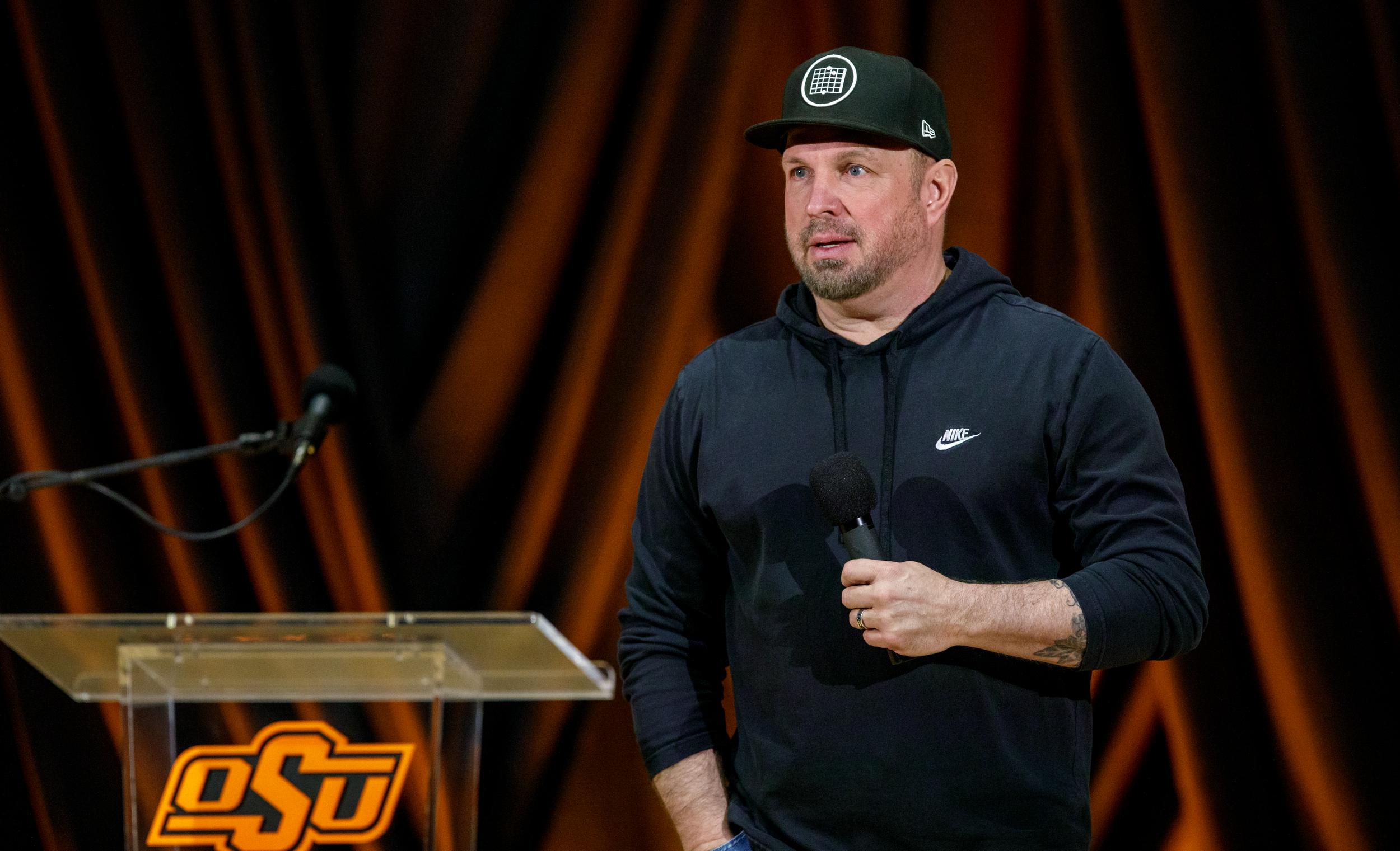 Garth Brooks stands with a microphone next to a lectern at a press conference