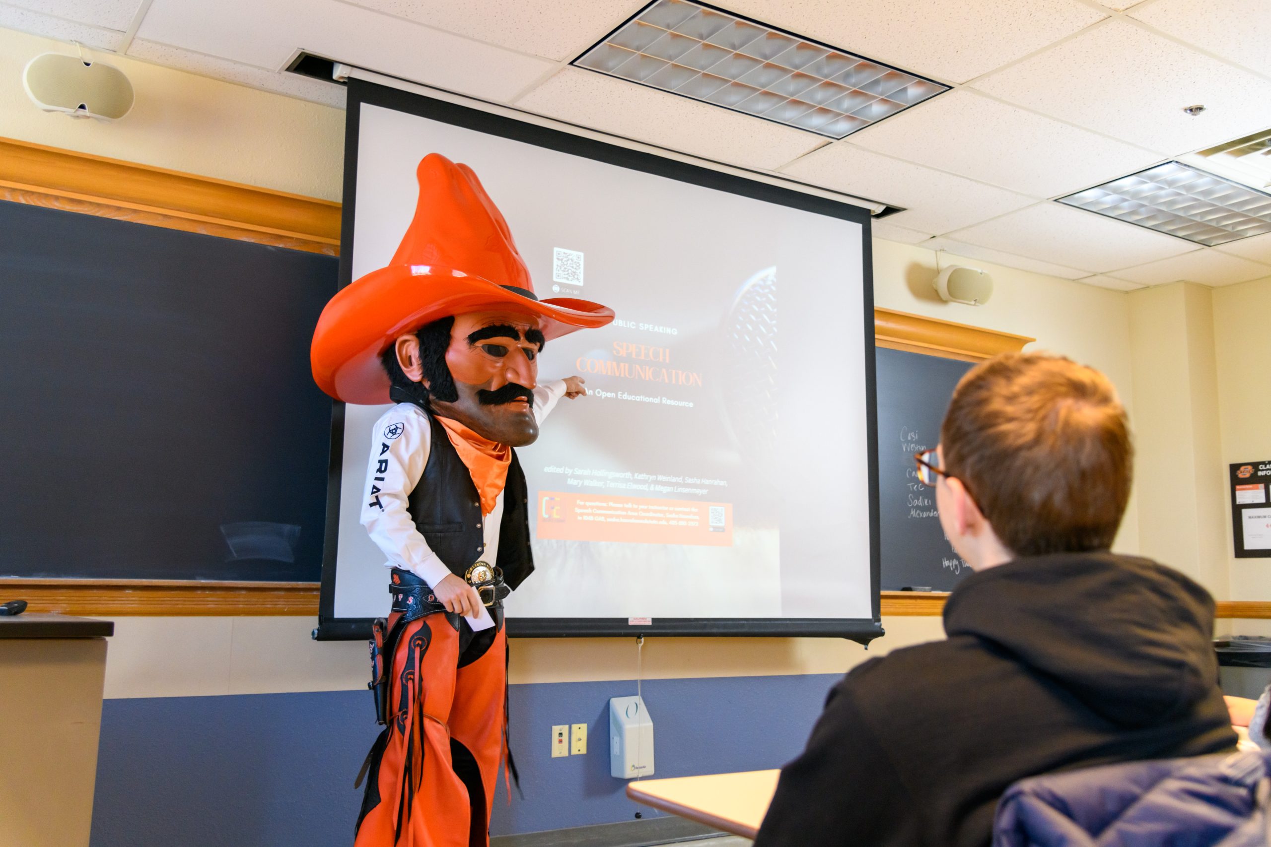 Pistol Pete is explaining to students about the speech communication minor and pointing to the projector