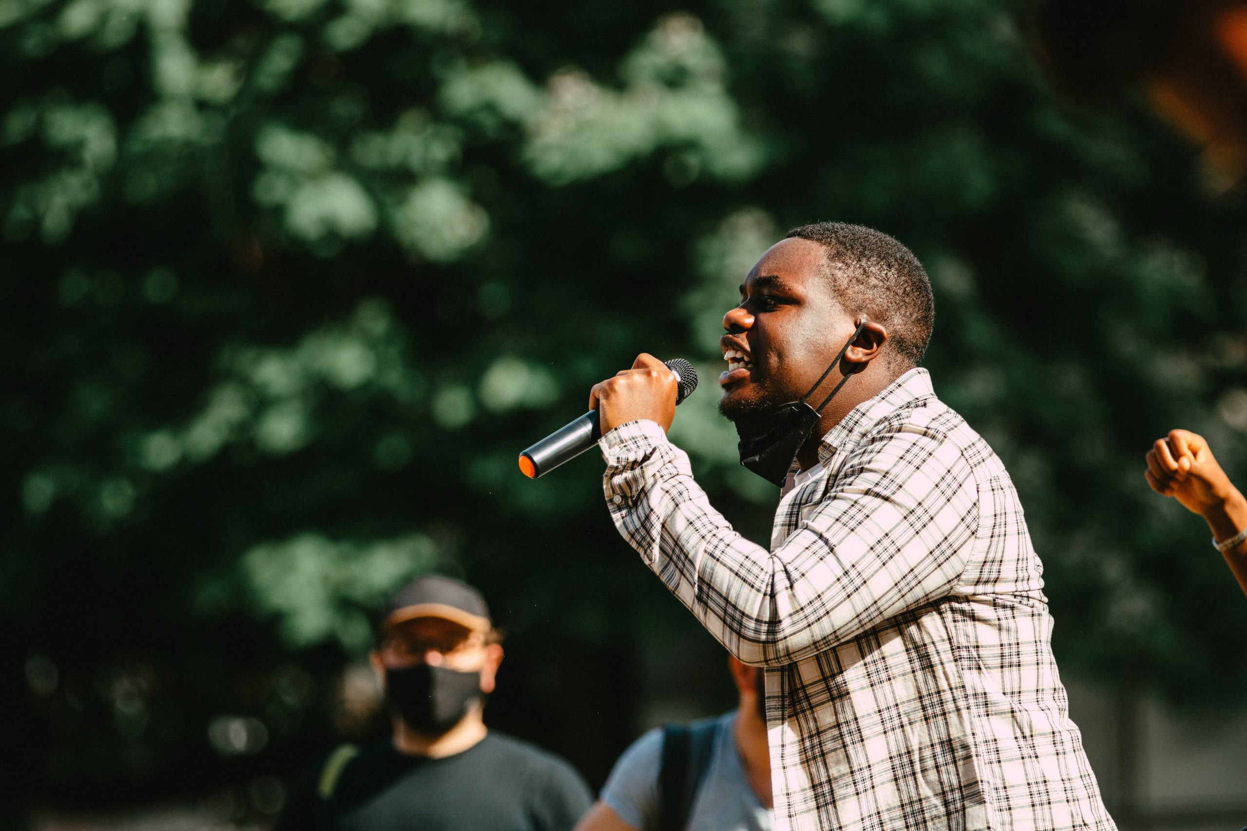 A young black man with a microphone passionately addresses an outdoor audience not in the picture