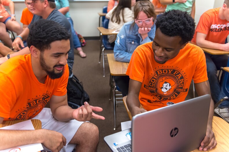 Two OSU students sitting at a laptop together discussing an assignment.