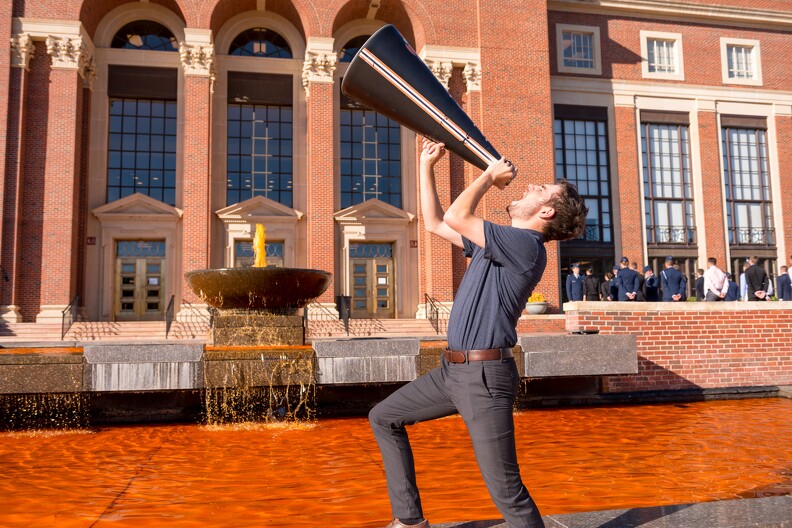 A young man uses a megaphone to deliver a message next to the orange dyed fountain in front of Edmon Low library.