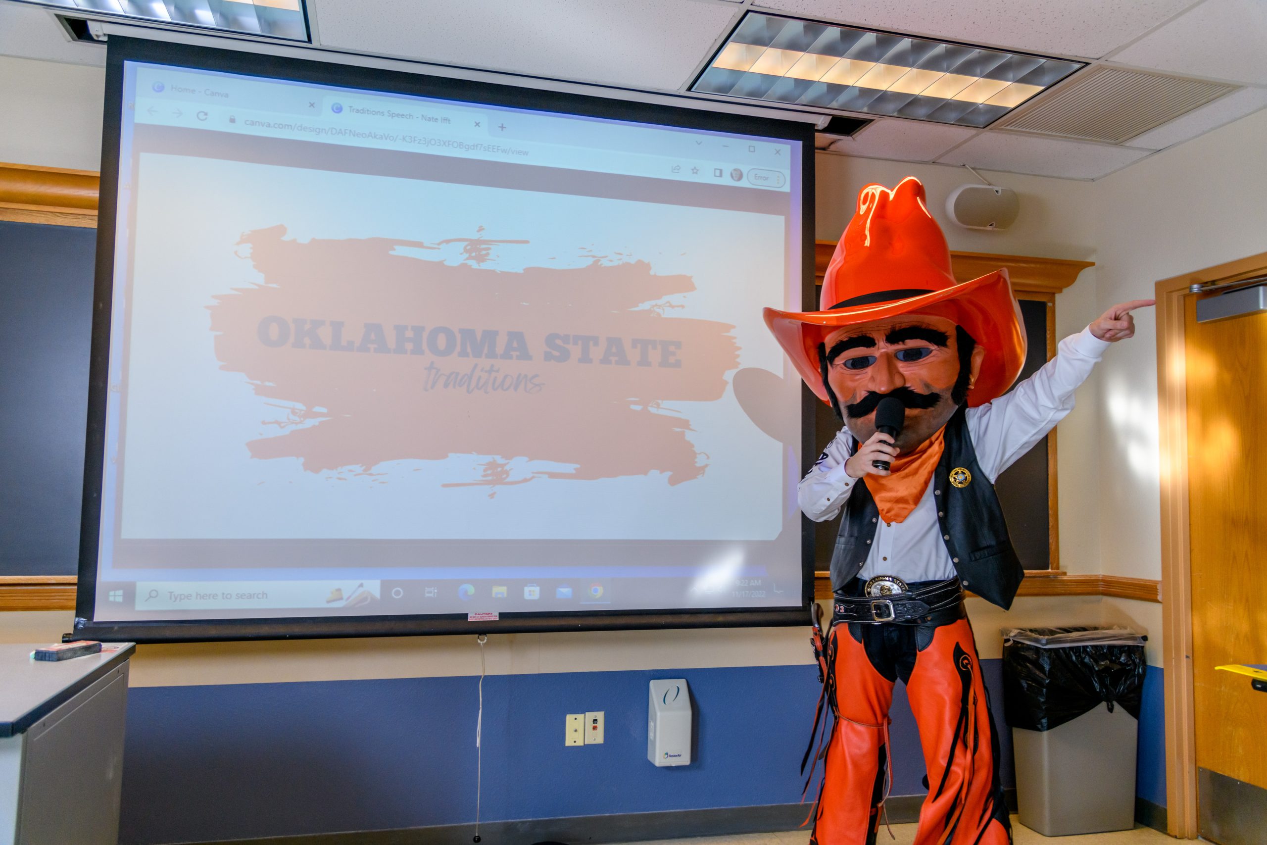 The OSU mascot, Pistol Pete stands at the front of a classroom holding a microphone while giving a presentation