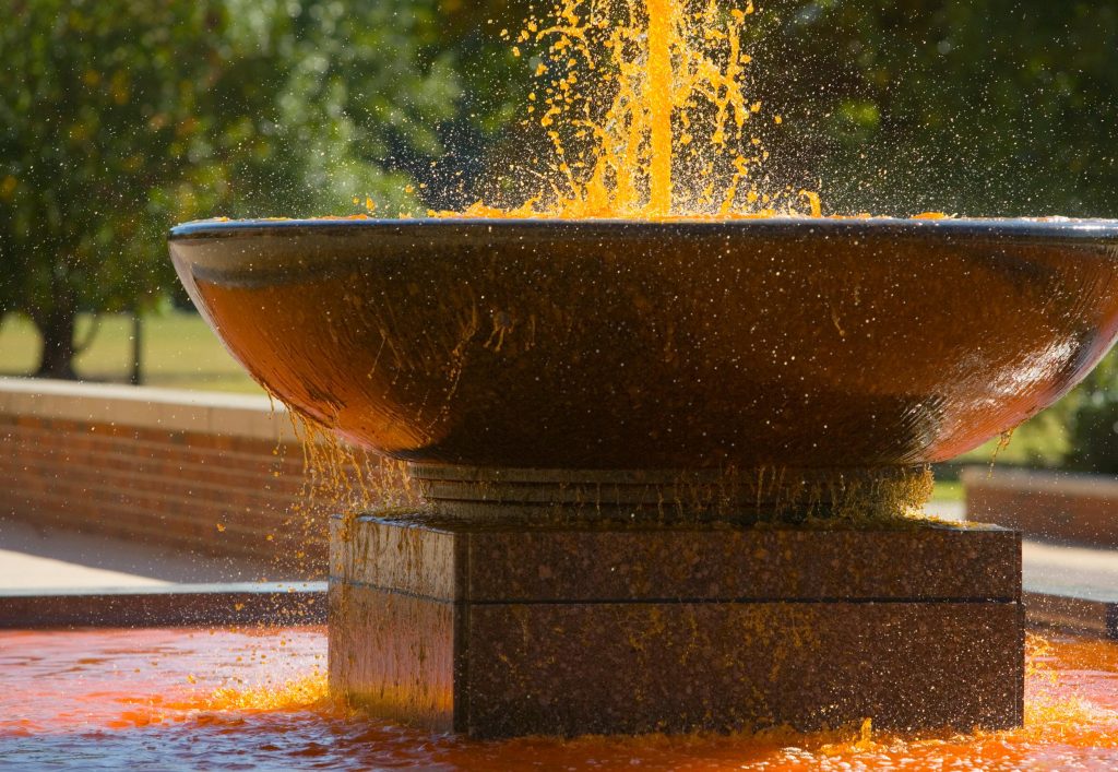 Photograph of the fountain in front of Edmon Low Library after it has been dyed orange for Oklahoma State University's annual Homecoming celebration.
