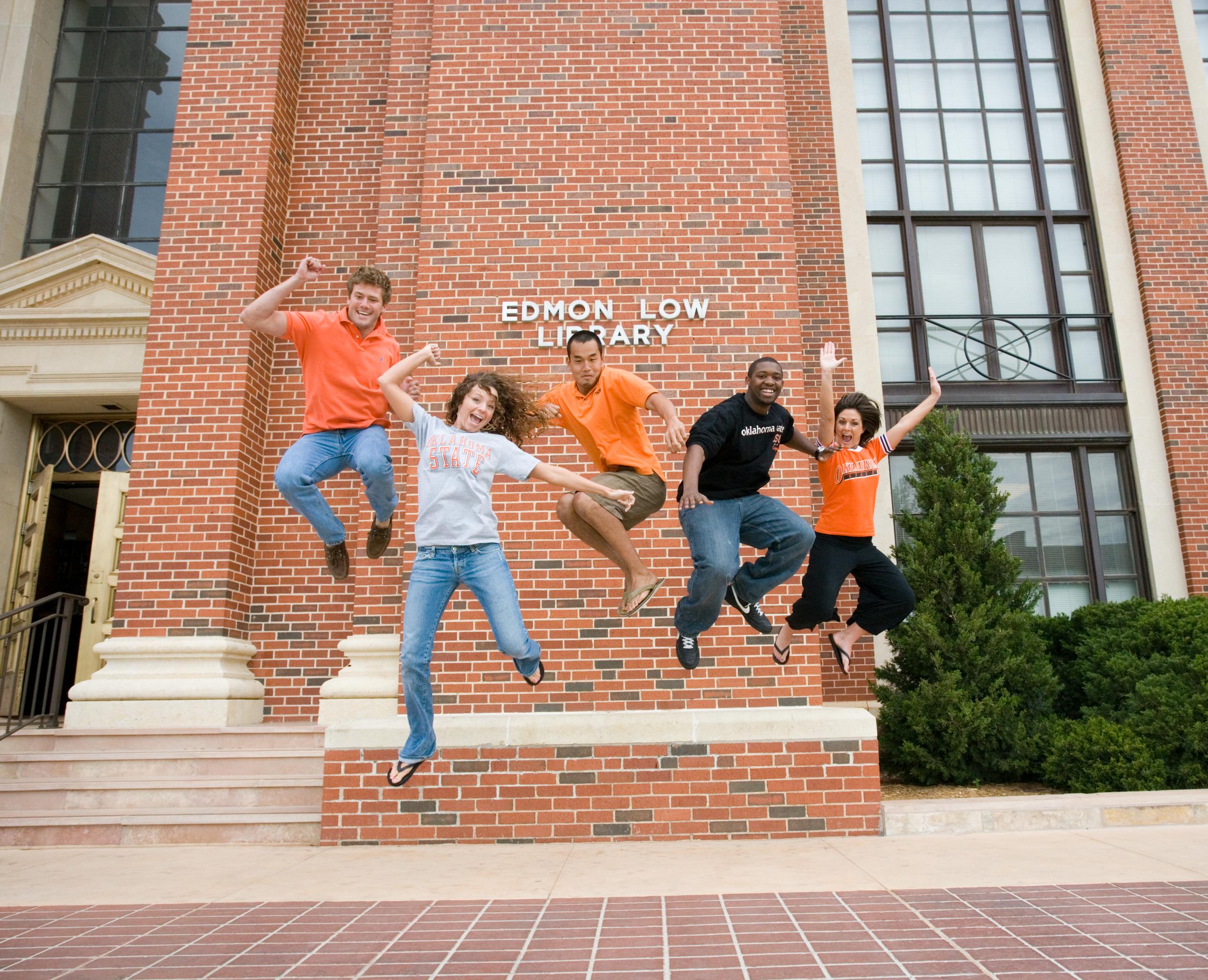 Five OSU students jumping up in the air in front of the Edmon Low Library