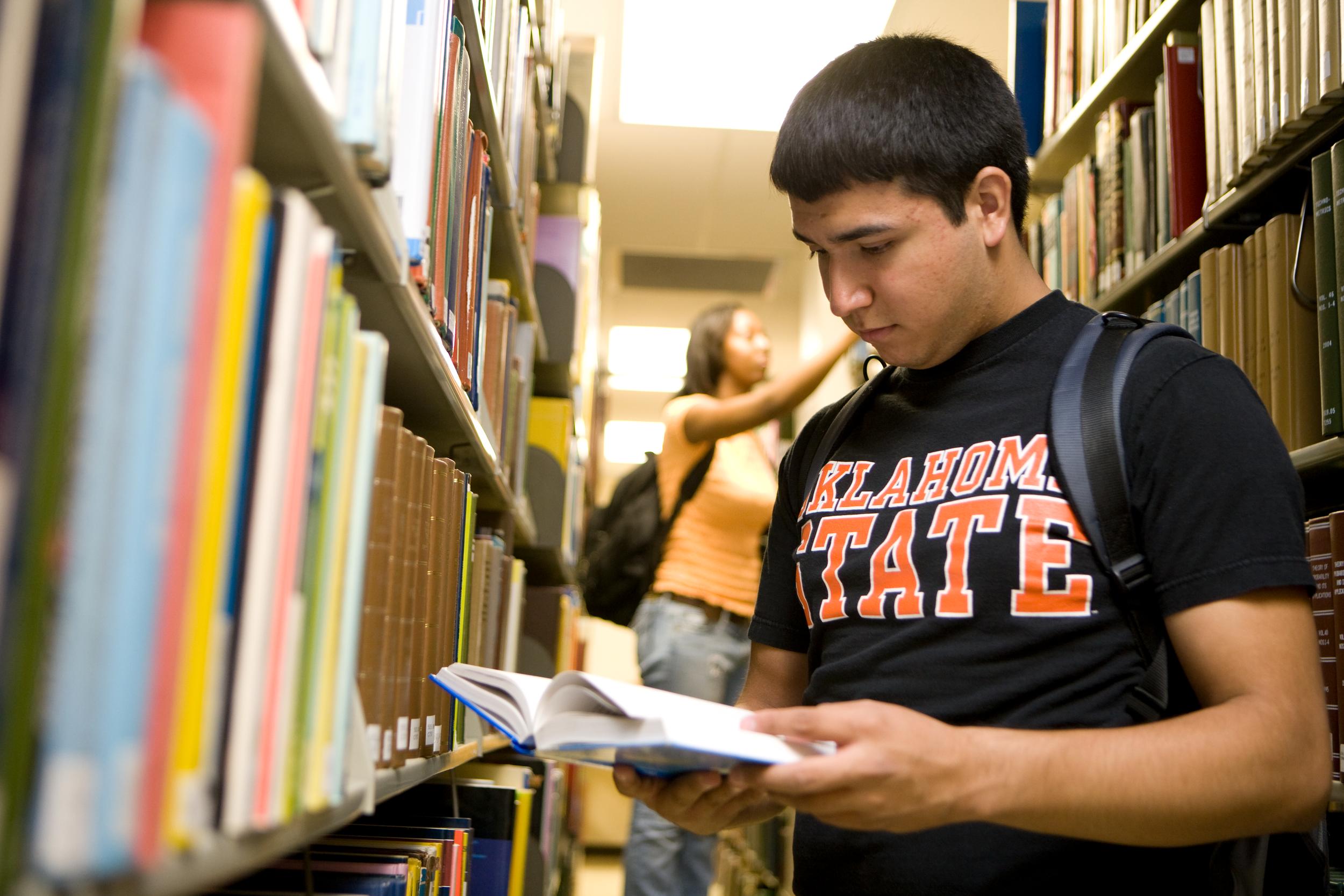 OSU student standing between two tall library shelves while reading a book