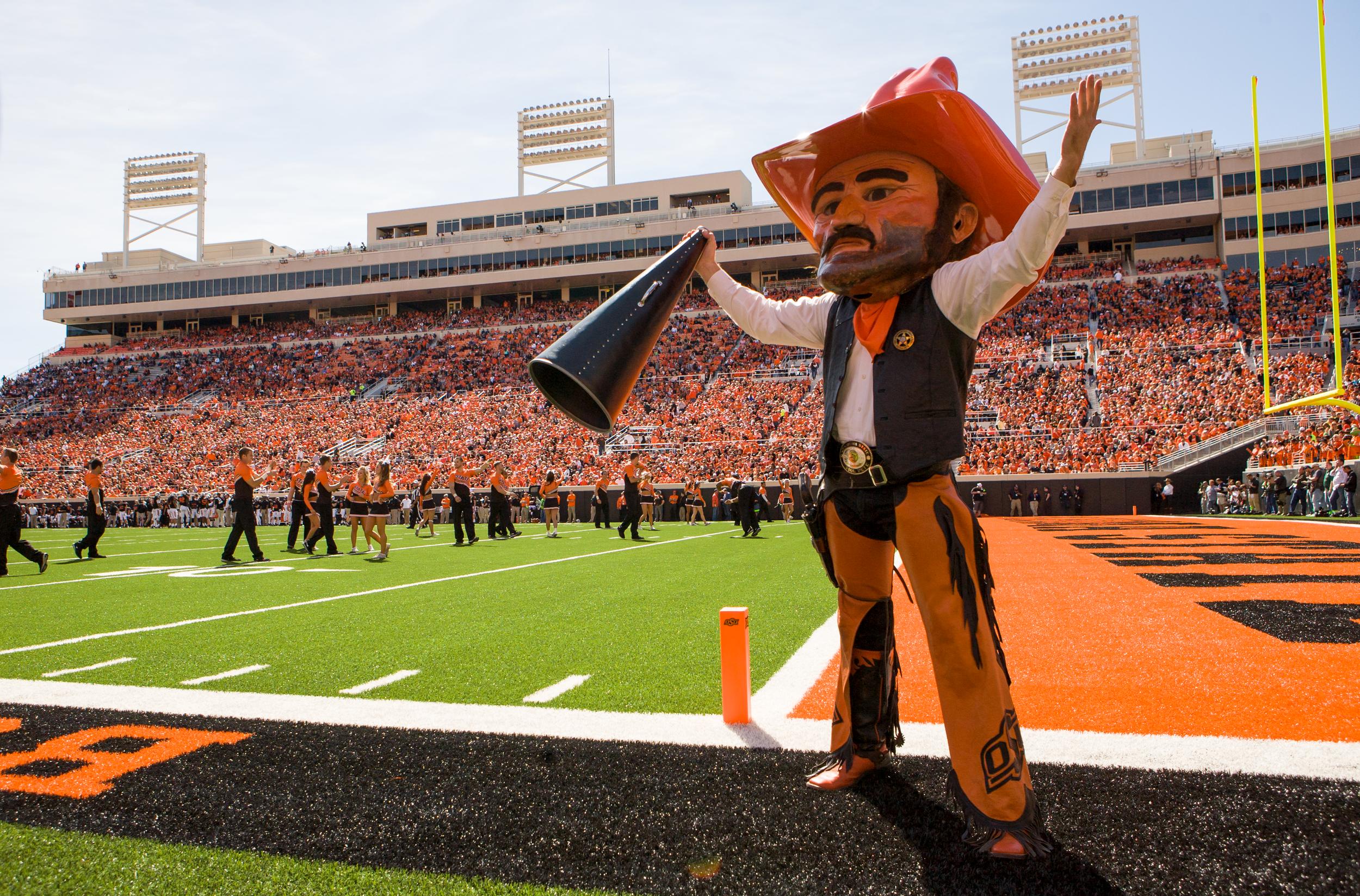 Pistol Pete stands in Boone Pickens Stadium raising one empty hand and a megaphone in the other hand.