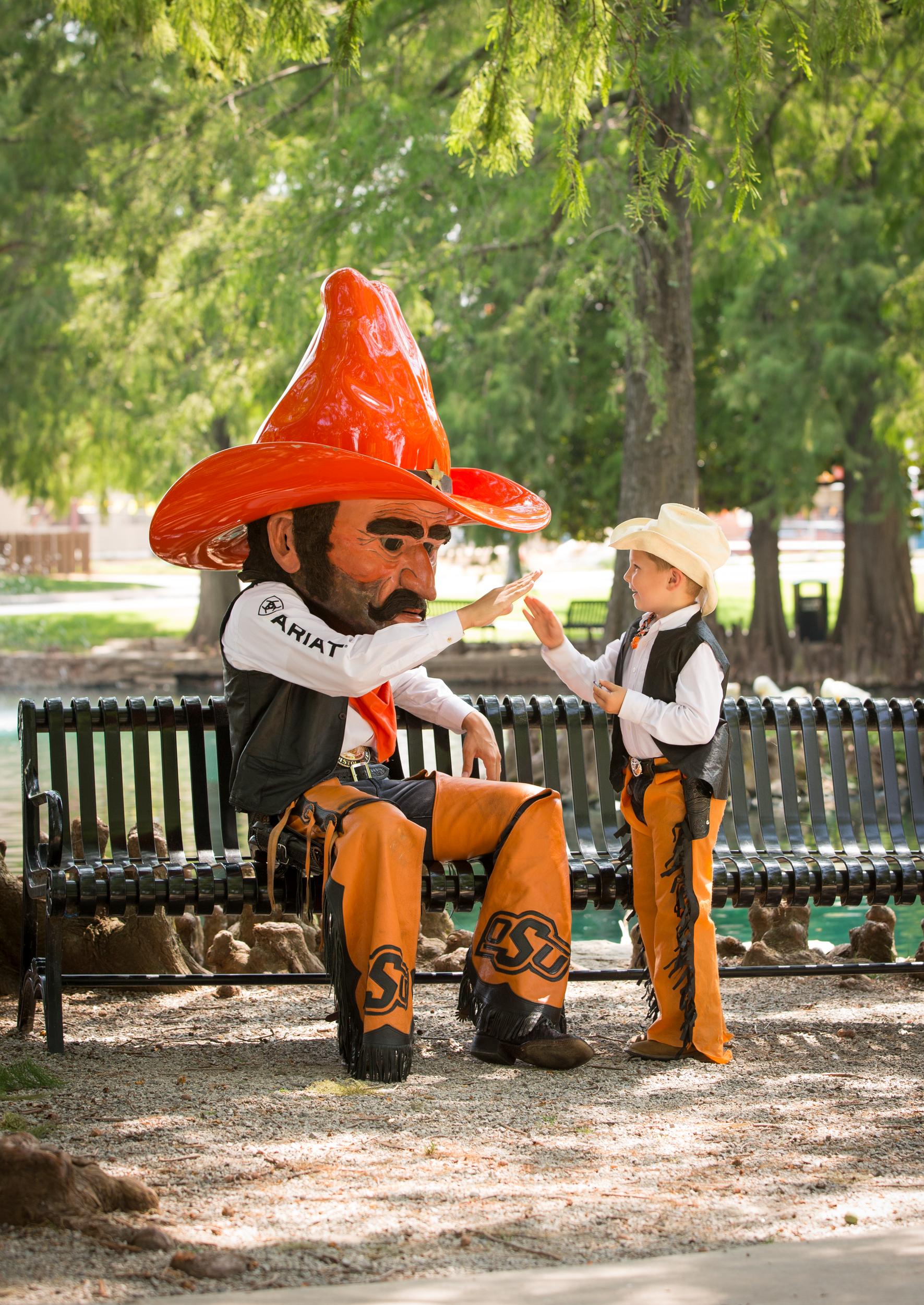 Pistol Pete sits on a bench near Theta pond while giving a young OSU fan dressed like him a high five.
