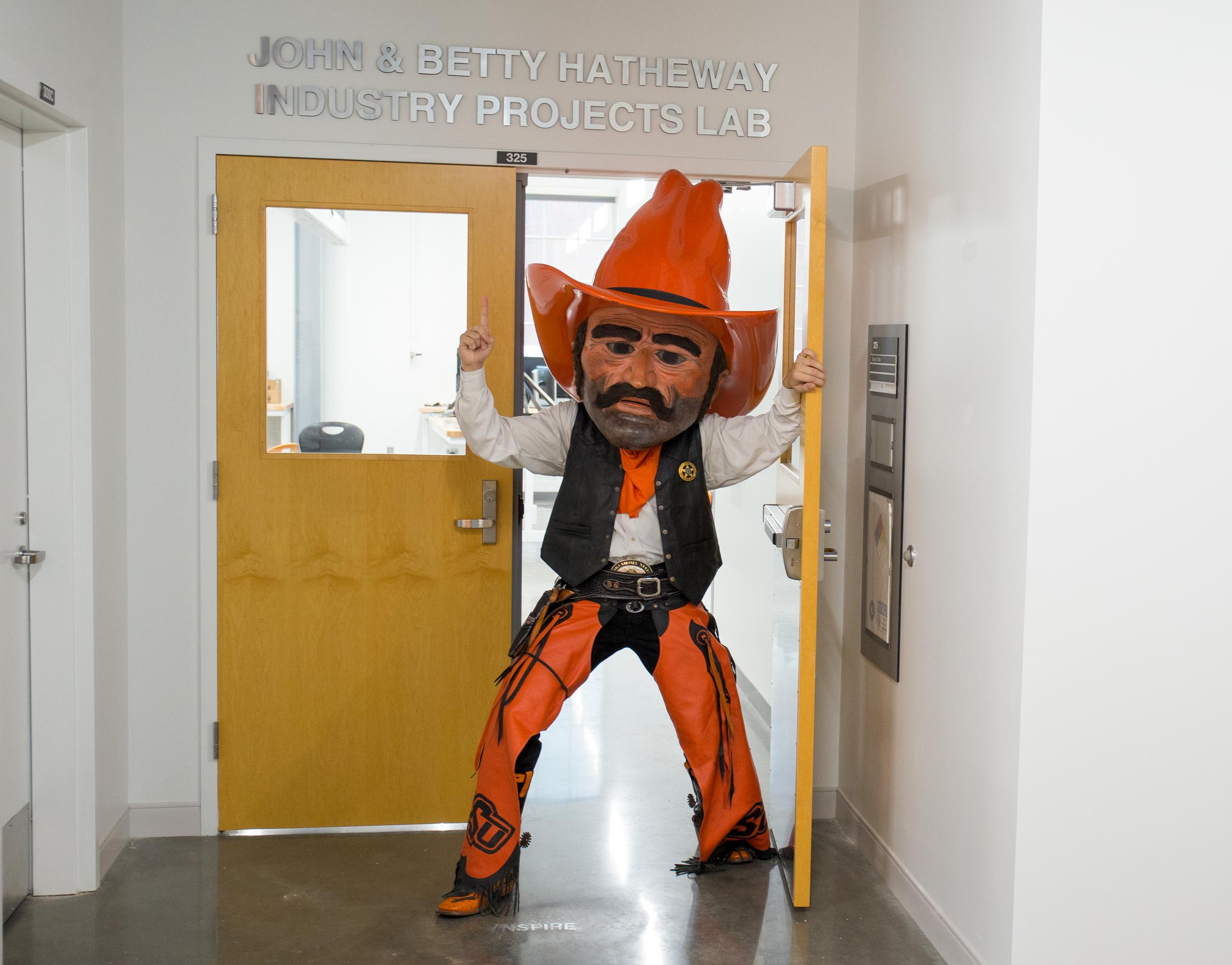 Pistol Pete walks through double doors while showing a number one gesture.