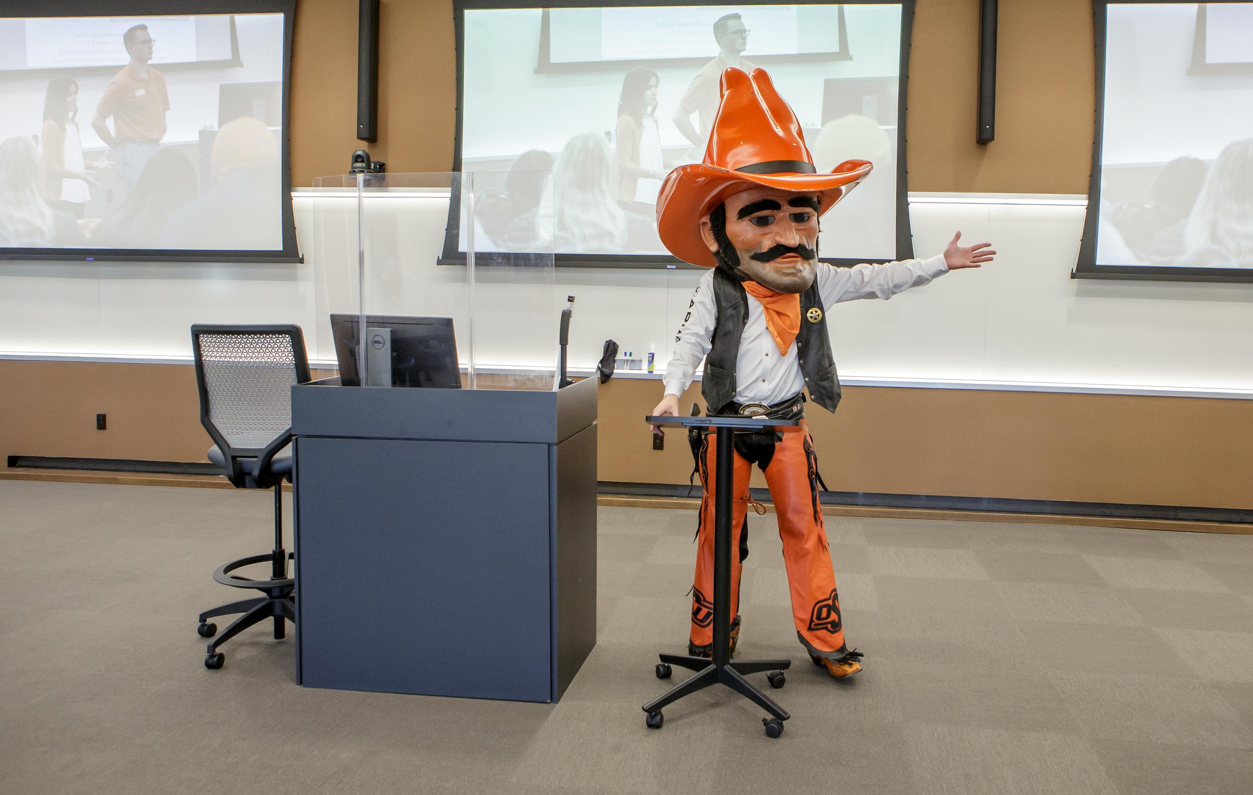 Pistol Pete is speaking to an audience and gesturing to his left by putting his arm out to the side.