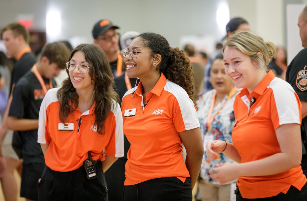 Three OSU students wearing orange and white shirts standing at a campus event