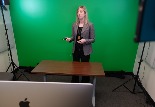 A young woman stands in front of a green screen while recording a video