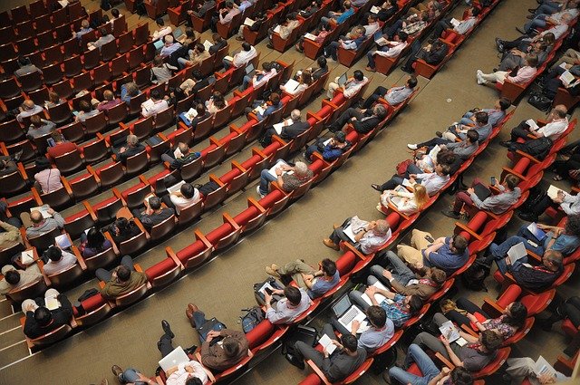 An overhead view of several people sitting in a large lecture hall.