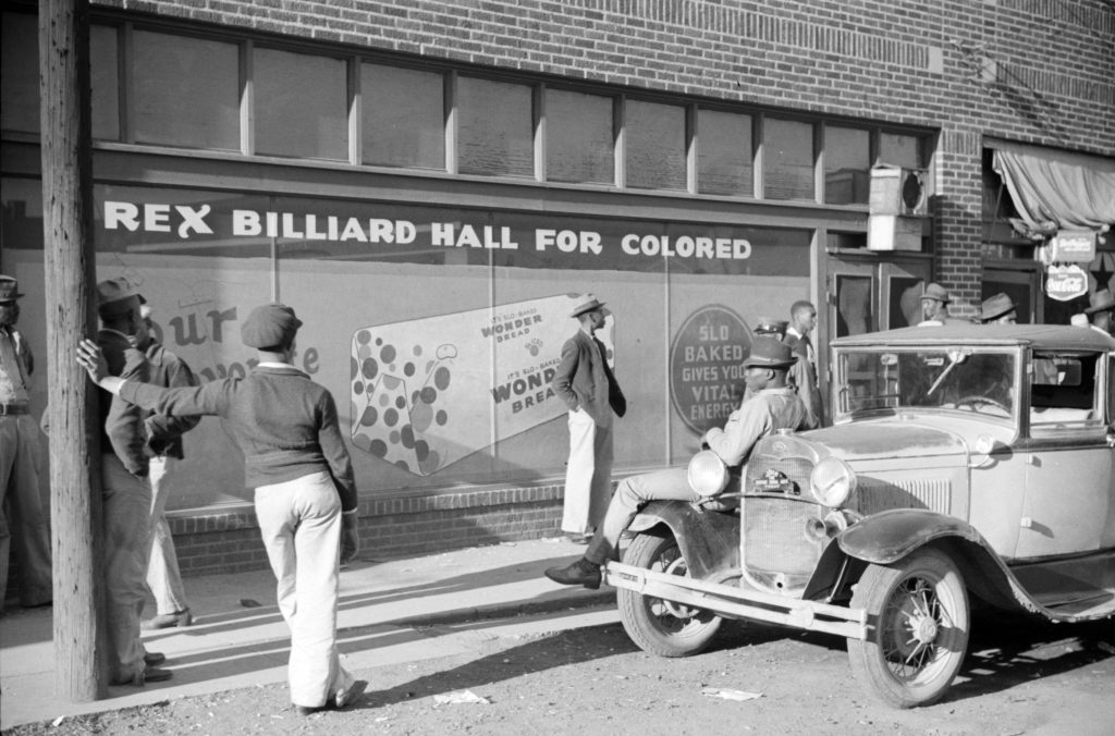 A black and white photograph of men standing in front of a business titled "Rex Billiard Hall for Colored"