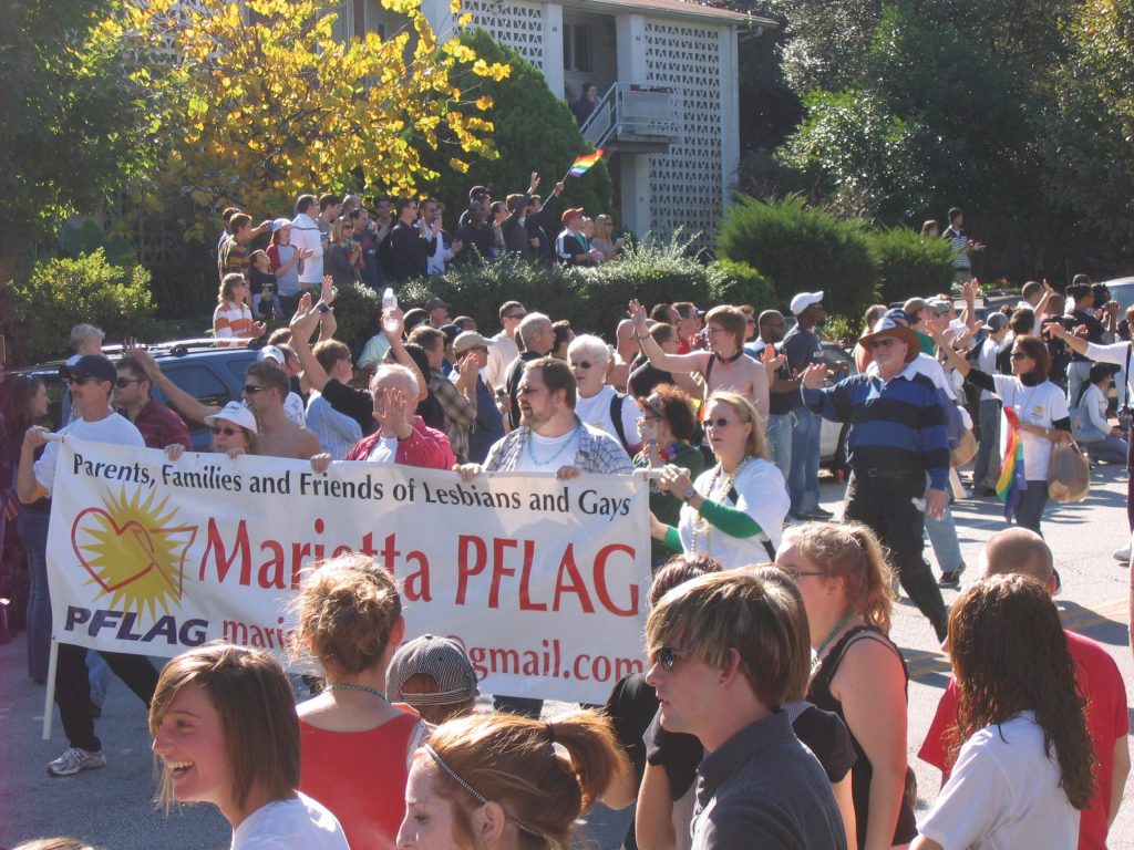 A group of individuals walking down a street holding a banner for the Marietta PFLAG organization.