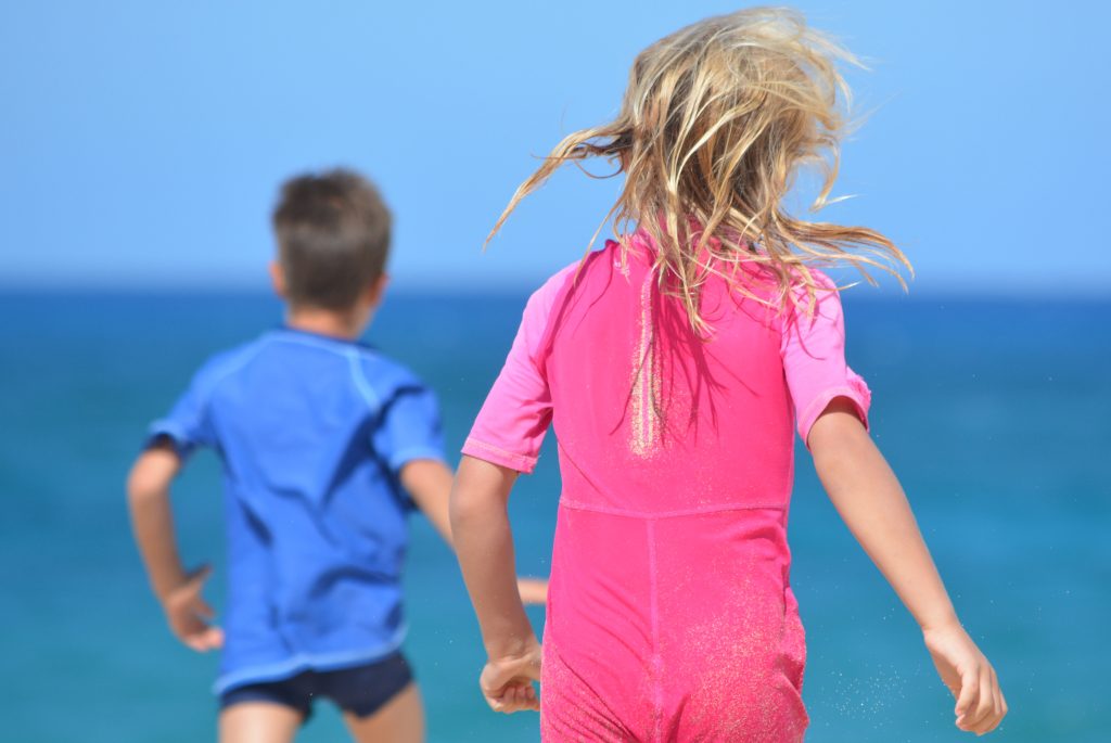 A boy wearing blue and a girl wearing pink running into the ocean.