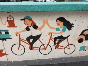 Street art depicting two people riding bikes and giving each other high fives