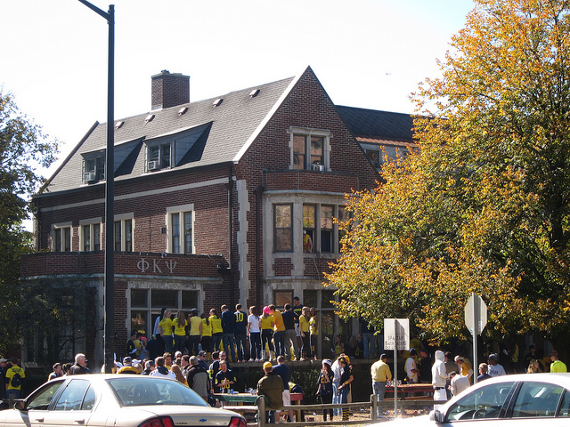 A group of college students standing in front of a fraternity.